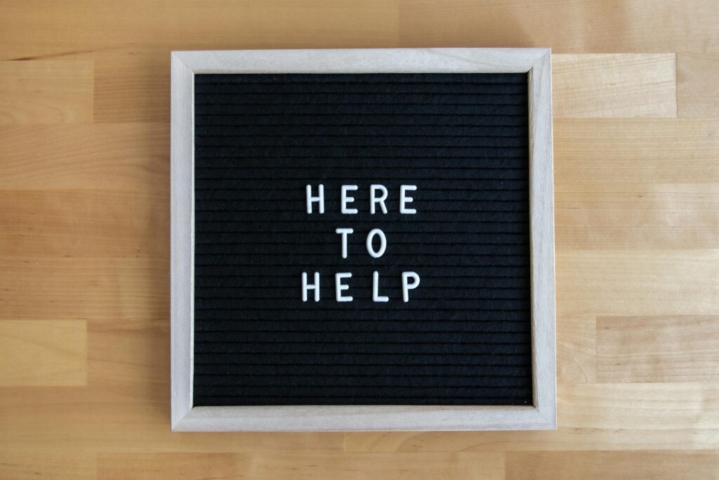 Black letter board with white text 'Here to Help' on a wooden background.