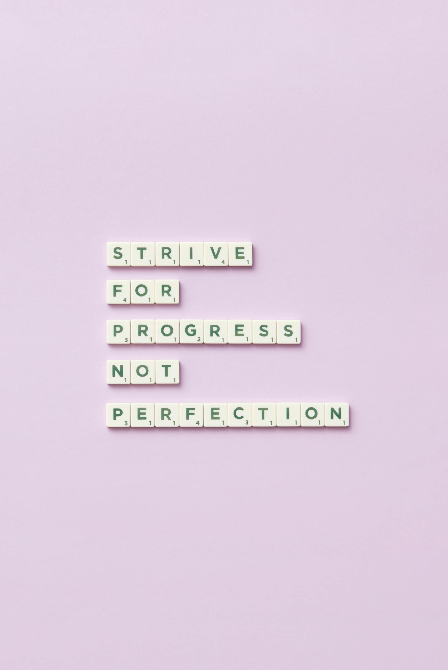 Scrabble tiles spelling 'Strive for progress, not perfection' on a pastel background.